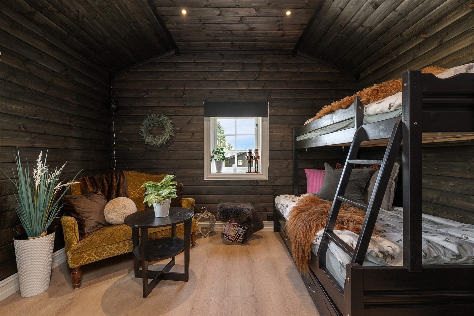 Et lunt og stemningsfullt soverom med mørkbeisede tømmervegger og koselig interiør. Rommet er innredet med en familiekøyeseng. Galleribilde