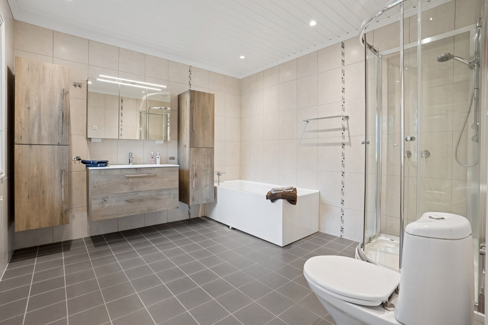 Flislagt bad ved hovedsoverommet utstyrt med servant med slette fronter, dusjkabinett og badekar. Galleribilde