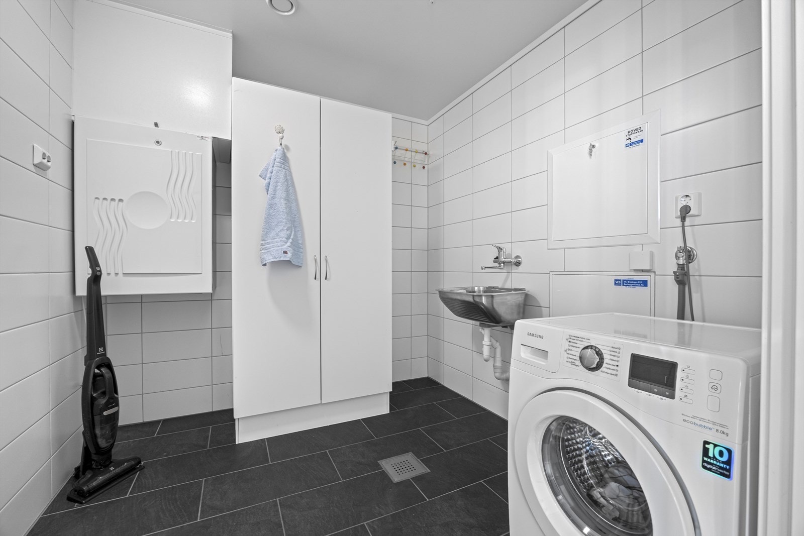 Romslig vaskerom med fliser til tak, opplegg for vaskemaskin og lintøyskap. Galleribilde