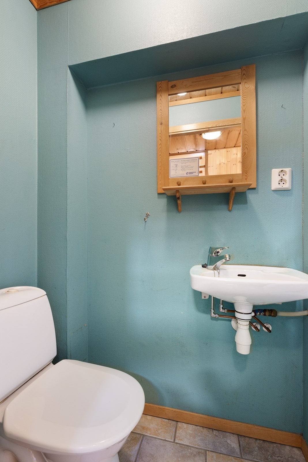 Toalettrom i 1. etasje, med flislagt gulv, gulvmontert toalett og vegghengt servant. Malt glassfiberstrie på vegger og panel i tak. Galleribilde