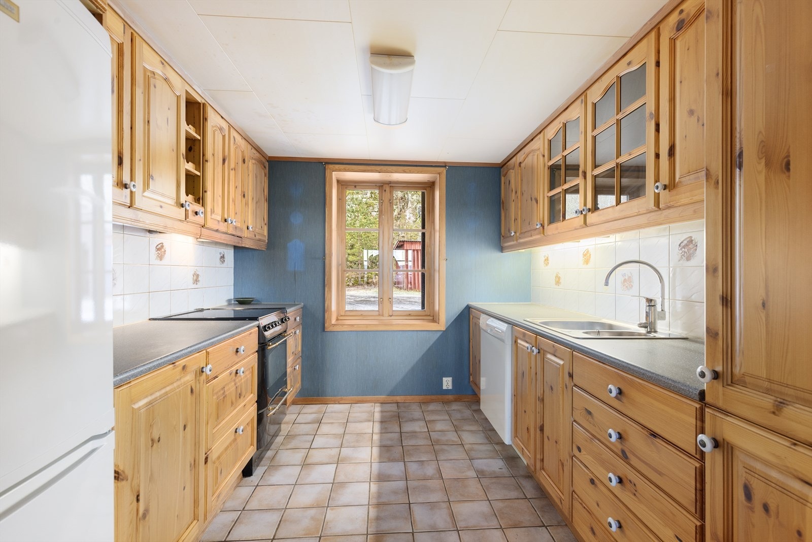 Kjøkkenet har flislagt gulv med varmekabler og takhøy kjøkkeninnredning fra 1999. Det er avsatt plass til frittstående hvitevarer. Galleribilde