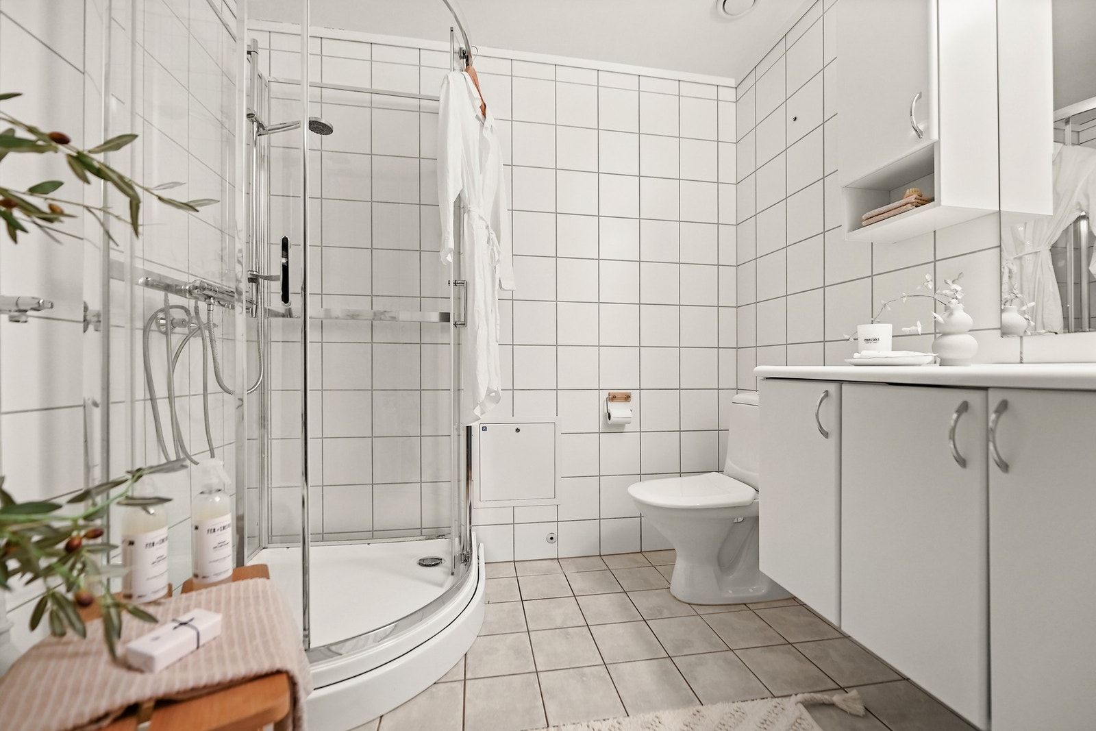 Boligen har et flislagt bad som også fungerer som vaskerom. Innredningen er holdt i lyse farger, gulvet er belagt med fliser og har varmekabler. Badet er innredet med dusjkabinett, servantskap, speil, gulvstående wc og opplegg for vaskemaskin. Galleribilde