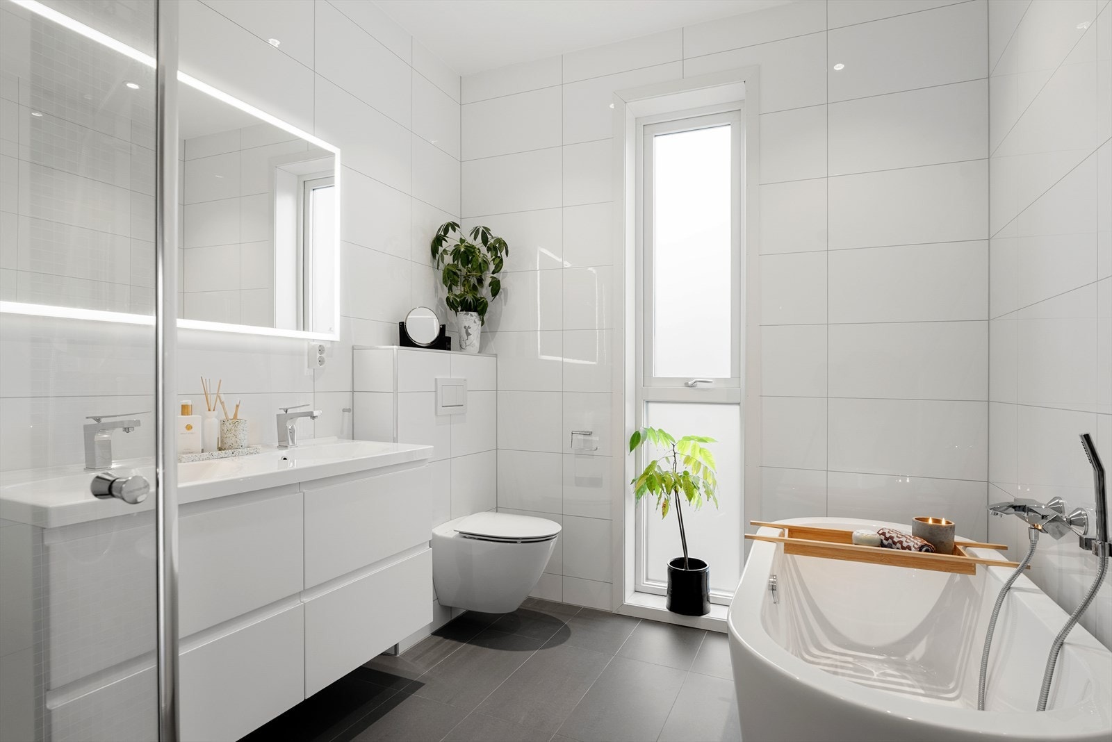 Boligen kan by på totalt to flotte bad - bad nr. 1 er innredet med hvit baderomsinnredning, veggmontert toalett, badekar og dusjhjørne med glassvegger Galleribilde