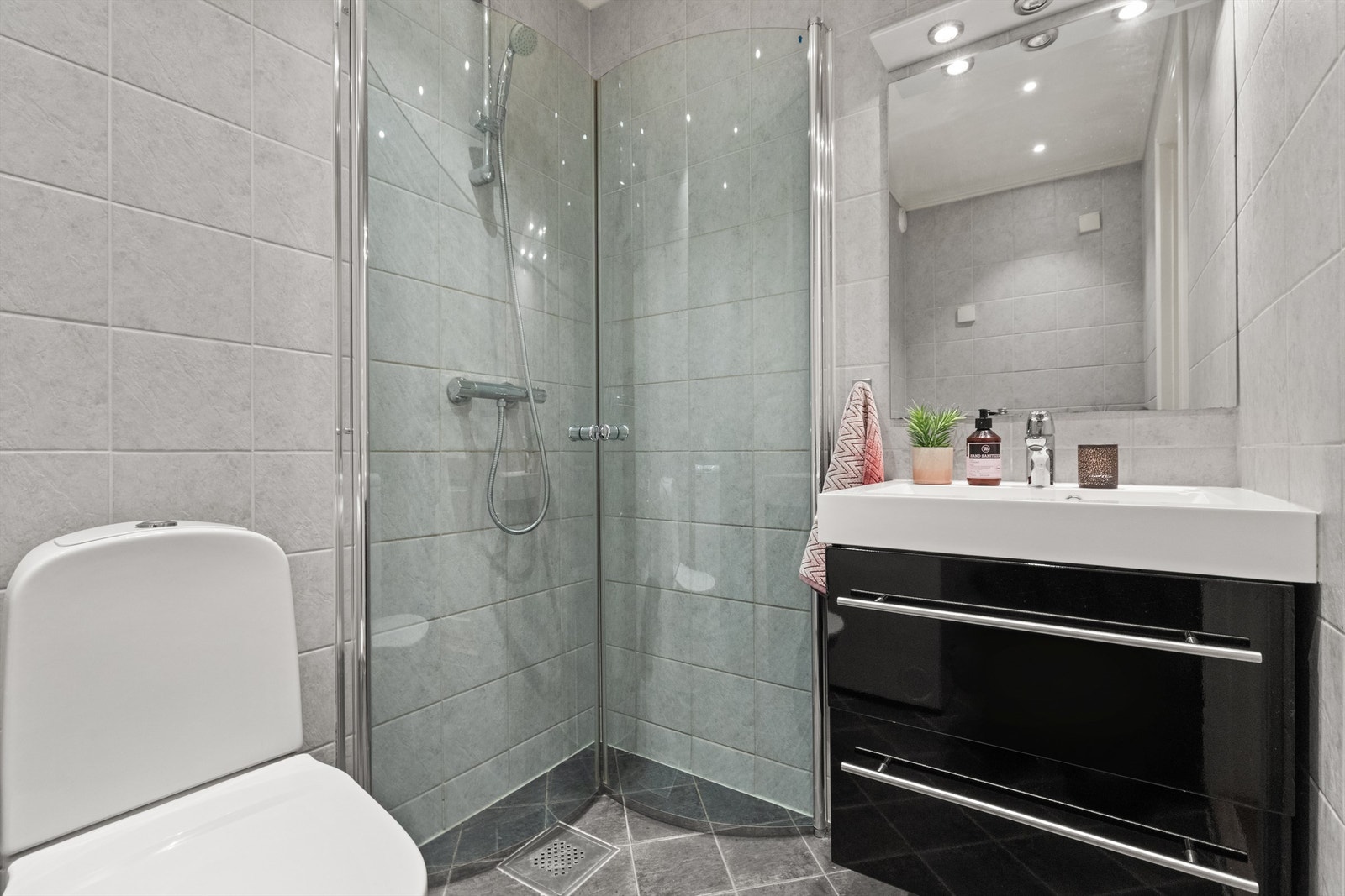 Badet er pent flislagt på gulv og vegger. Innredet med klosett, servant nedfelt i innredning og dusjhjørne med svingbare glassdører. Galleribilde