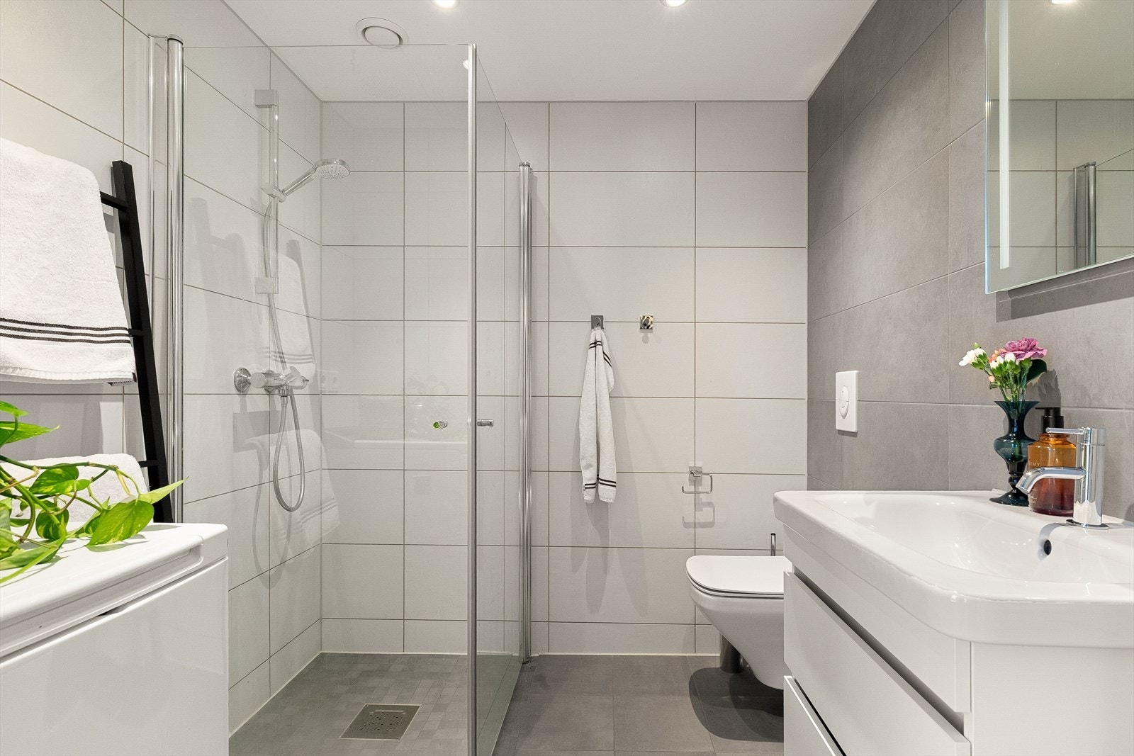 Et lyst og moderne flislagt baderom fra byggeår 2019. Baderommet har lysegrå fliser på gulv med vannbåren gulvvarme, store fine fliser på veggene og downlights i himlingen. Galleribilde