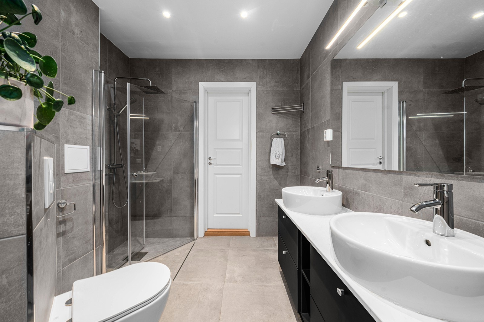 Rommet er videre innredet med nedsenket dusjhjørne med glassdører i herdet glass, vegghengt toalett og dobbel servant med underskap og speil med integrert belysning Galleribilde