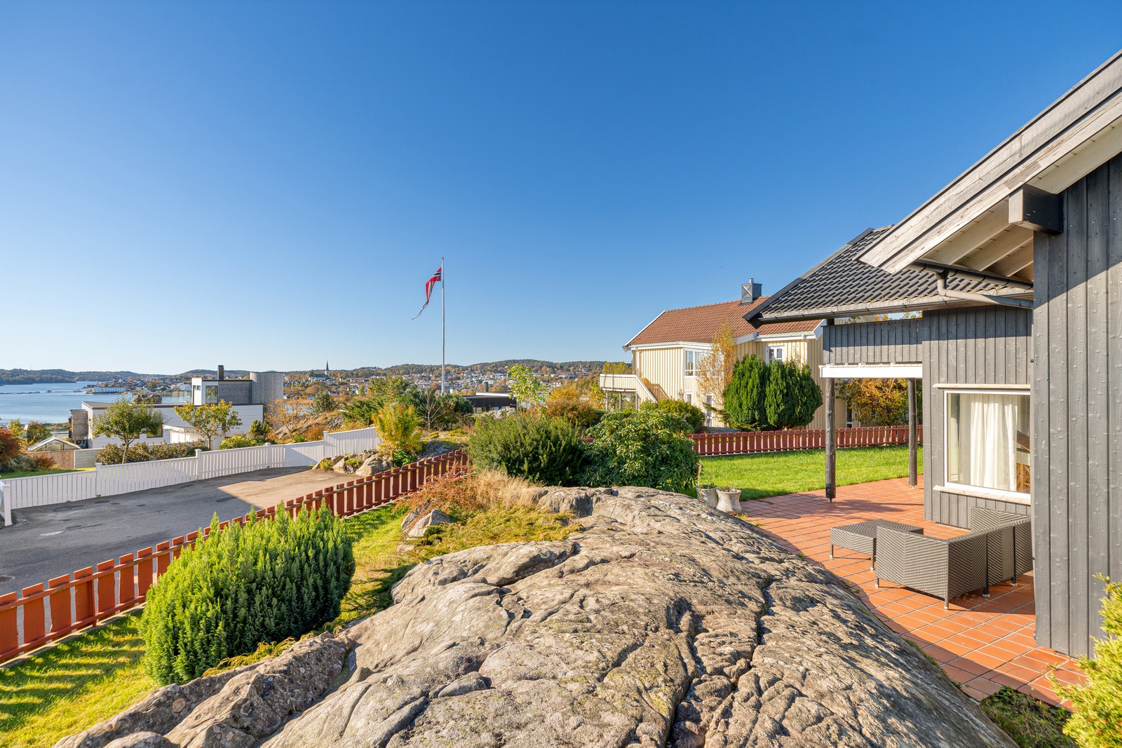 Utsikt fra hagen med fjord, flaggstang og steinformasjoner. Galleribilde