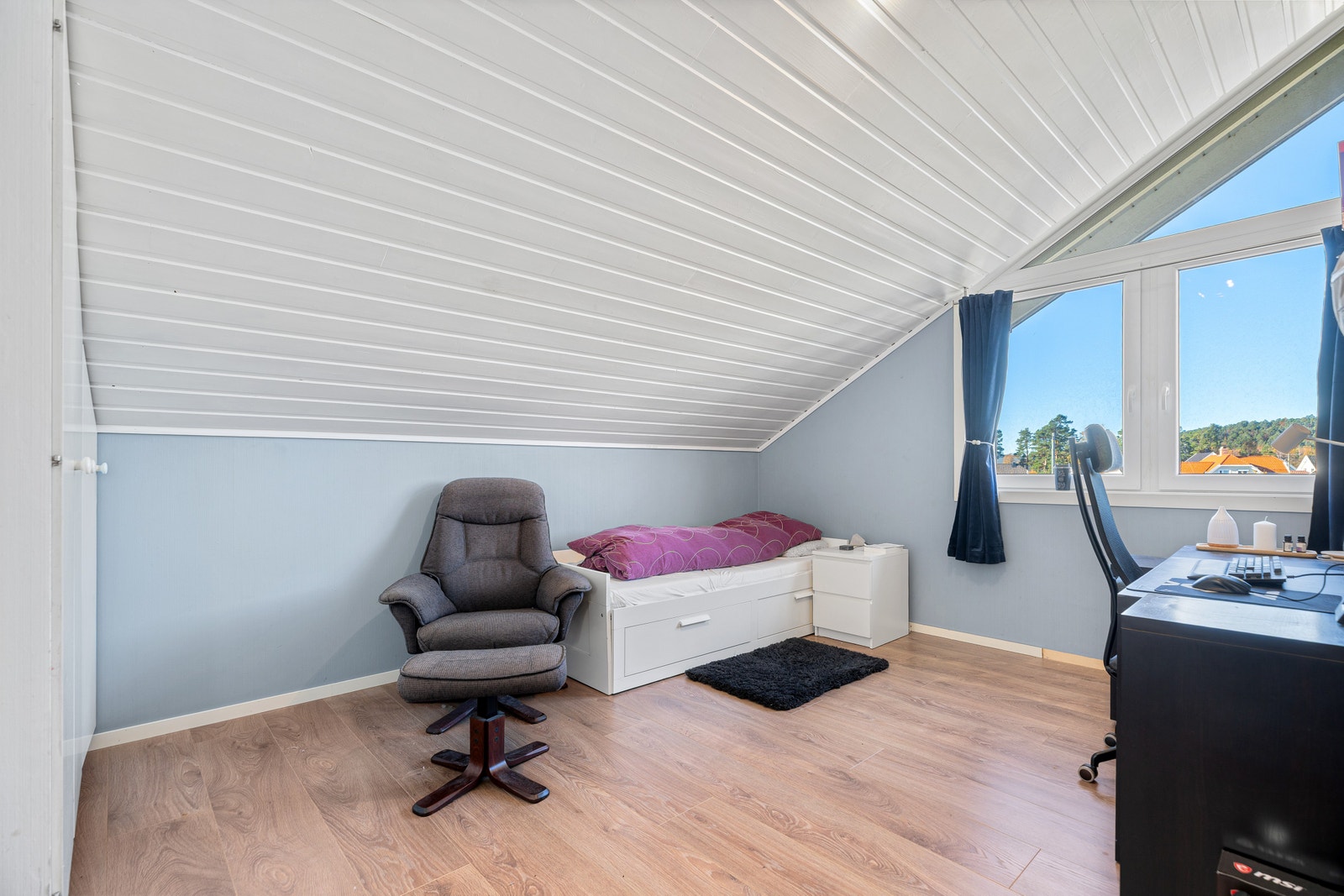 Soverom med seng, reclinerstol og kontorplass under skråtak. Galleribilde