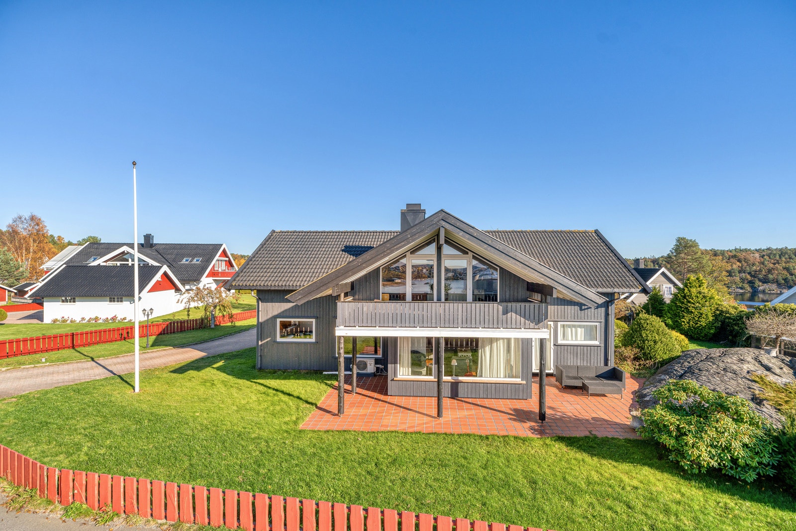 Eneboligens fasade mot hagen – grå kledning, store vinduer, plen og beplantning. Galleribilde