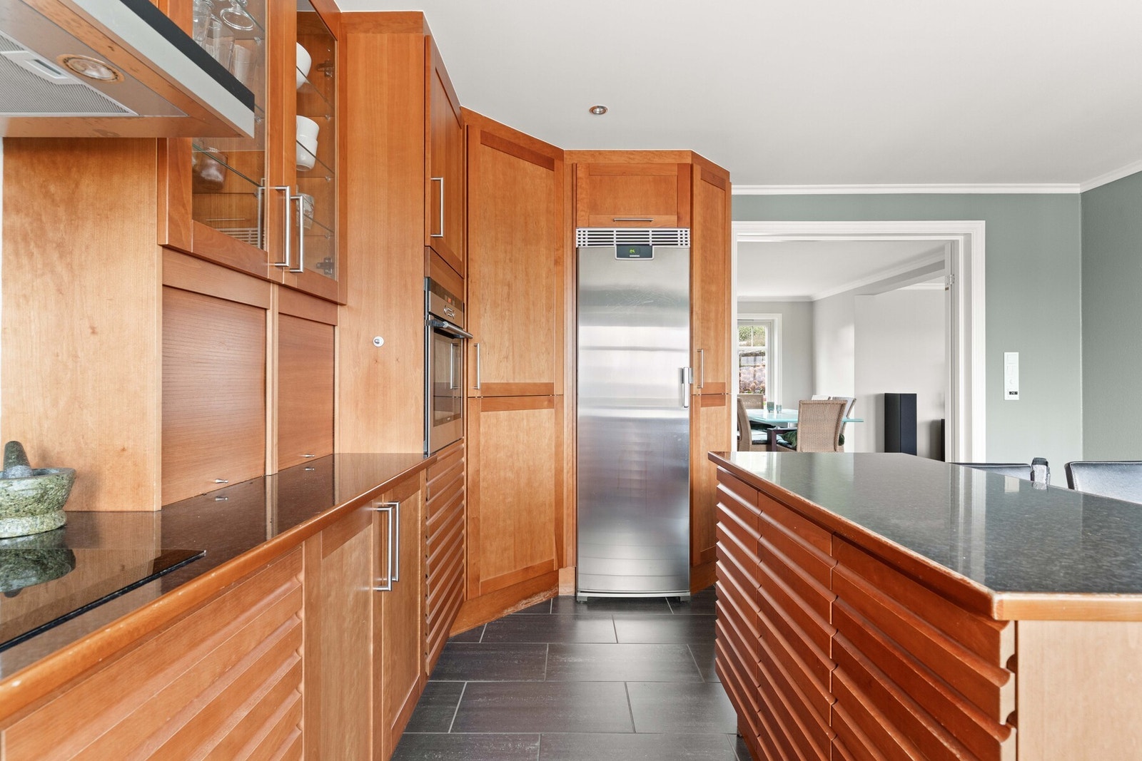 Dimbare downlights i taket tilfører ekstra lys til arbeidsflatene. Integrert i innredningen finner man platetopp, oppvaskmaskin og stekeovn i høyskap. Galleribilde