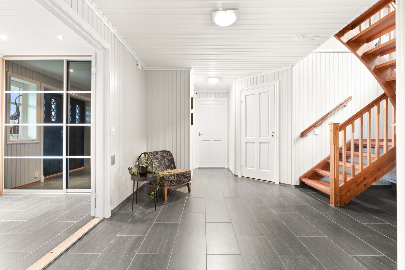 Langs begge kortveggene har entreen plassbygde skyvedørsgarderober med sorte speilfronter. Videre skilles entréen og hallen av dobble glassdører. Galleribilde