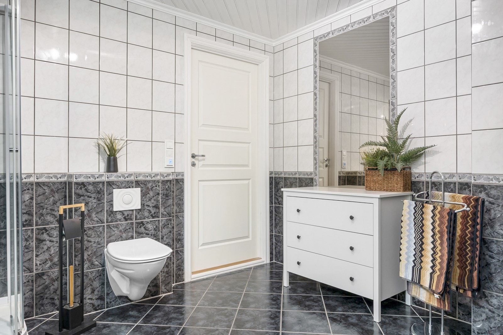 Badet er romslig med helflisede vegger og varmekabler i gulvet. Innredningen består av en servant nedfelt i benkeskap, speilskap med lys, vegghengt toalett og dusjkabinett. Her er det tilrettelagt for høy komfort i hverdagen. Galleribilde