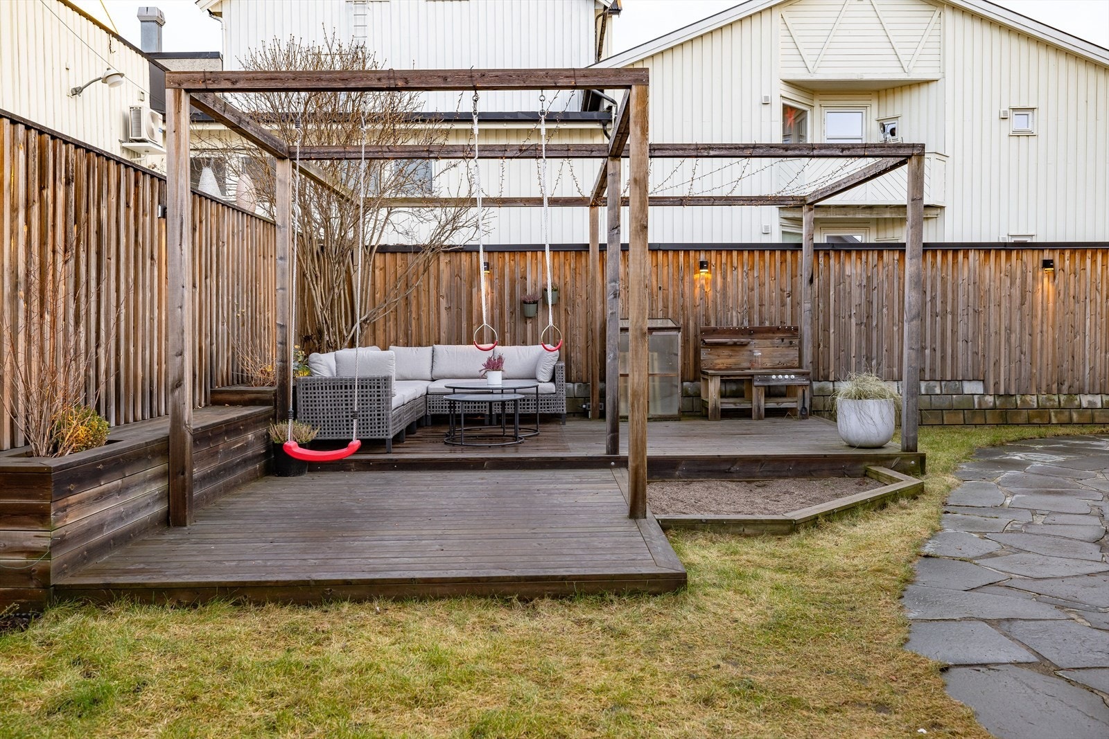 Hyggelig og skjermet bakgård med romslig terrasseplatting med innfelte blomsterkasser og sandkasse. Galleribilde