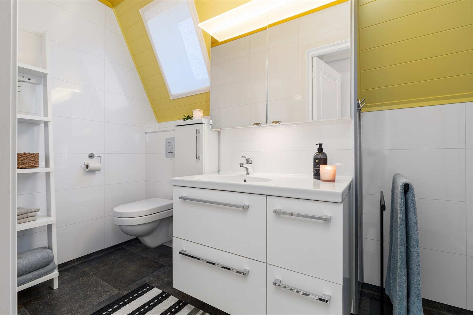 Bad på loft har vinylbelegg på gulv med varmekabel, våtromsplater på vegger og malt panel i tak | badet er utstyrt med baderomsinnredning, vegghengt wc og dusjkabinett Galleribilde