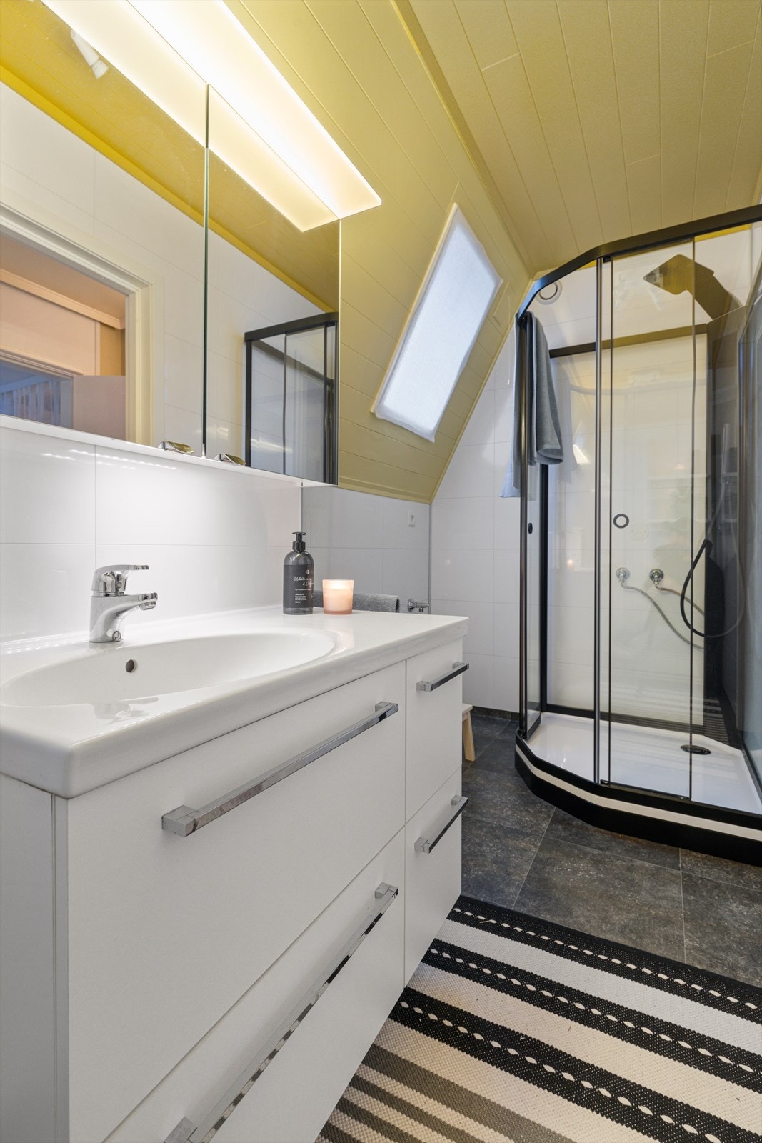 Bad på loft har vinylbelegg på gulv med varmekabel, våtromsplater på vegger og malt panel i tak | badet er utstyrt med baderomsinnredning, vegghengt wc og dusjkabinett Galleribilde