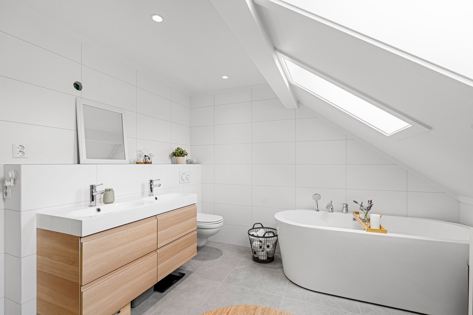 Delikat og moderne bad i 2 etasje med lyse fliser, innredning i eik og dobbel vask, badekar og takvindu Galleribilde