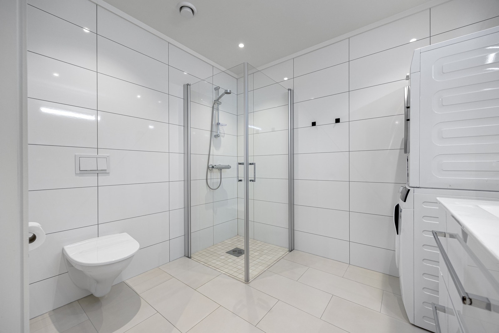 Badet er utstyrt med vegghengt servantinnredning, toalett, dusjhjørne, opplegg til vaskemaskin og speil med overlys. Det er varmekabler i gulvet. Galleribilde