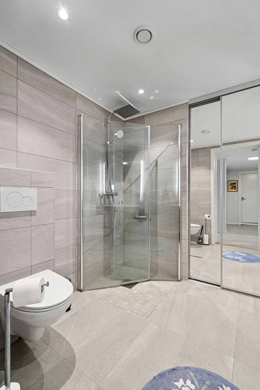 Badet er utstyrt med veggmontert toalett, innredning med servant, dusjhjørne med glassvegger og opplegg for vaskemaskin - en praktisk løsning som gjør rommet svært funksjonelt. Galleribilde