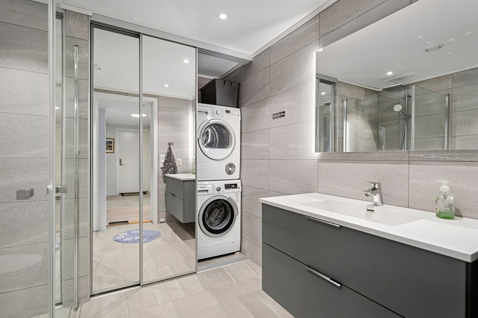 Boligens kombinerte bad og vaskerom, oppført i 2022, fremstår som stilrent og praktisk med gjennomgående moderne materialvalg. Gulvet er flislagt og har varmekabler som gir behagelig komfort året rundt. Galleribilde