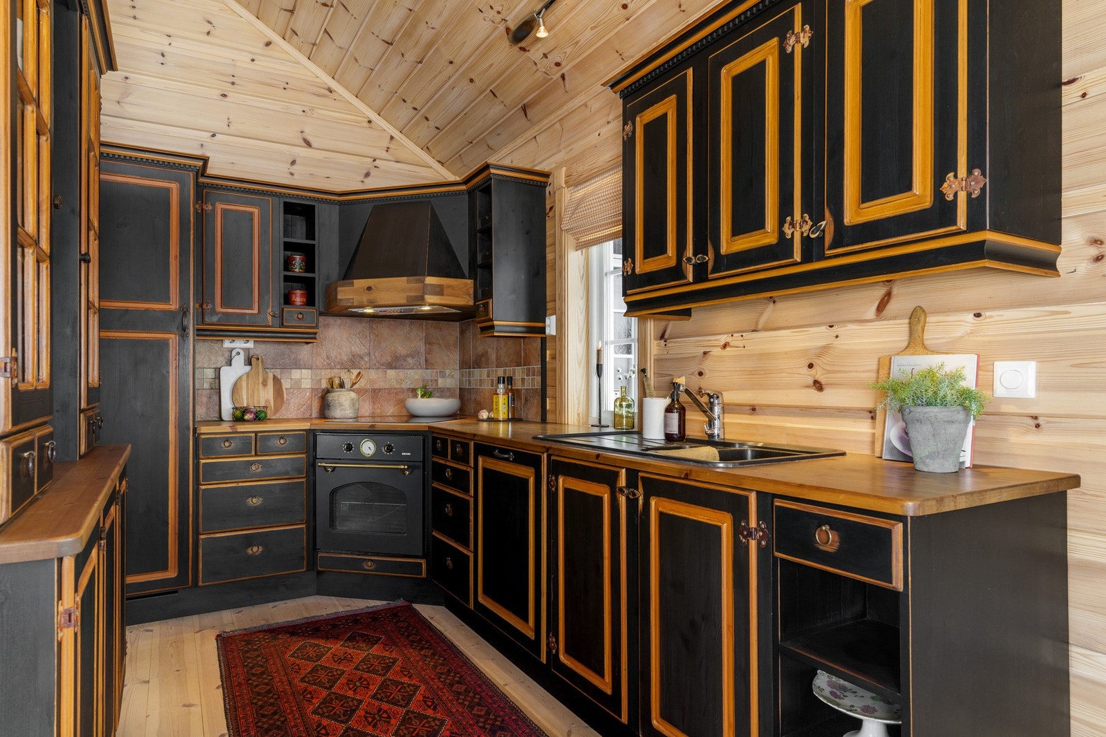Heltre sort hyttekjøkken med aldringsmalte skrog og fronter med integrerte hvitevarer. Det er også installert kjøkkenventilator med avtrekk ut. Galleribilde