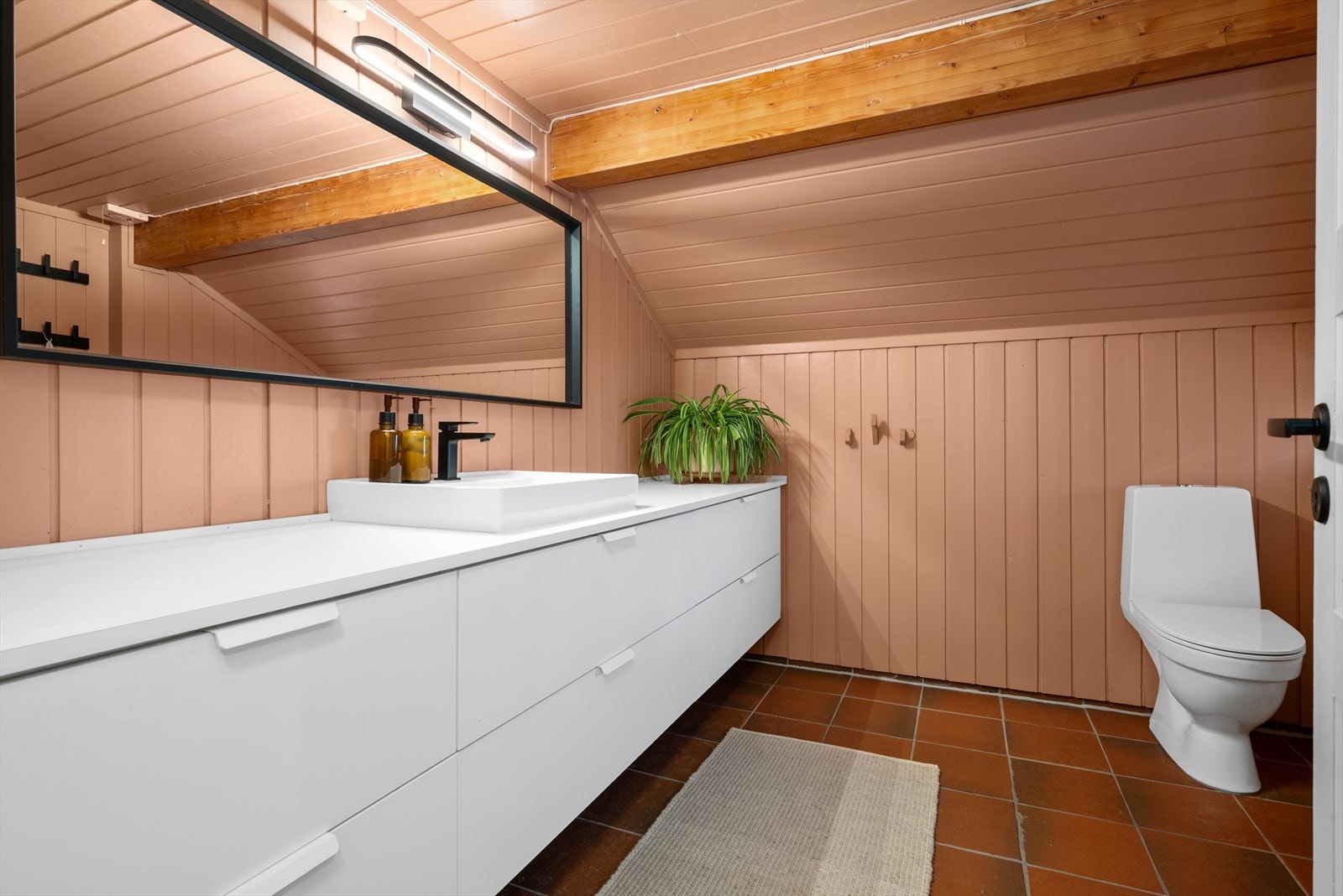 Drageren på badet er beholdt umalt, noe som skaper en lun atmosfære sammen med resten av den moderne innredningen. Baderomsmøblet løper langs hele langveggen og gir god oppbevaring for hele familien. Galleribilde