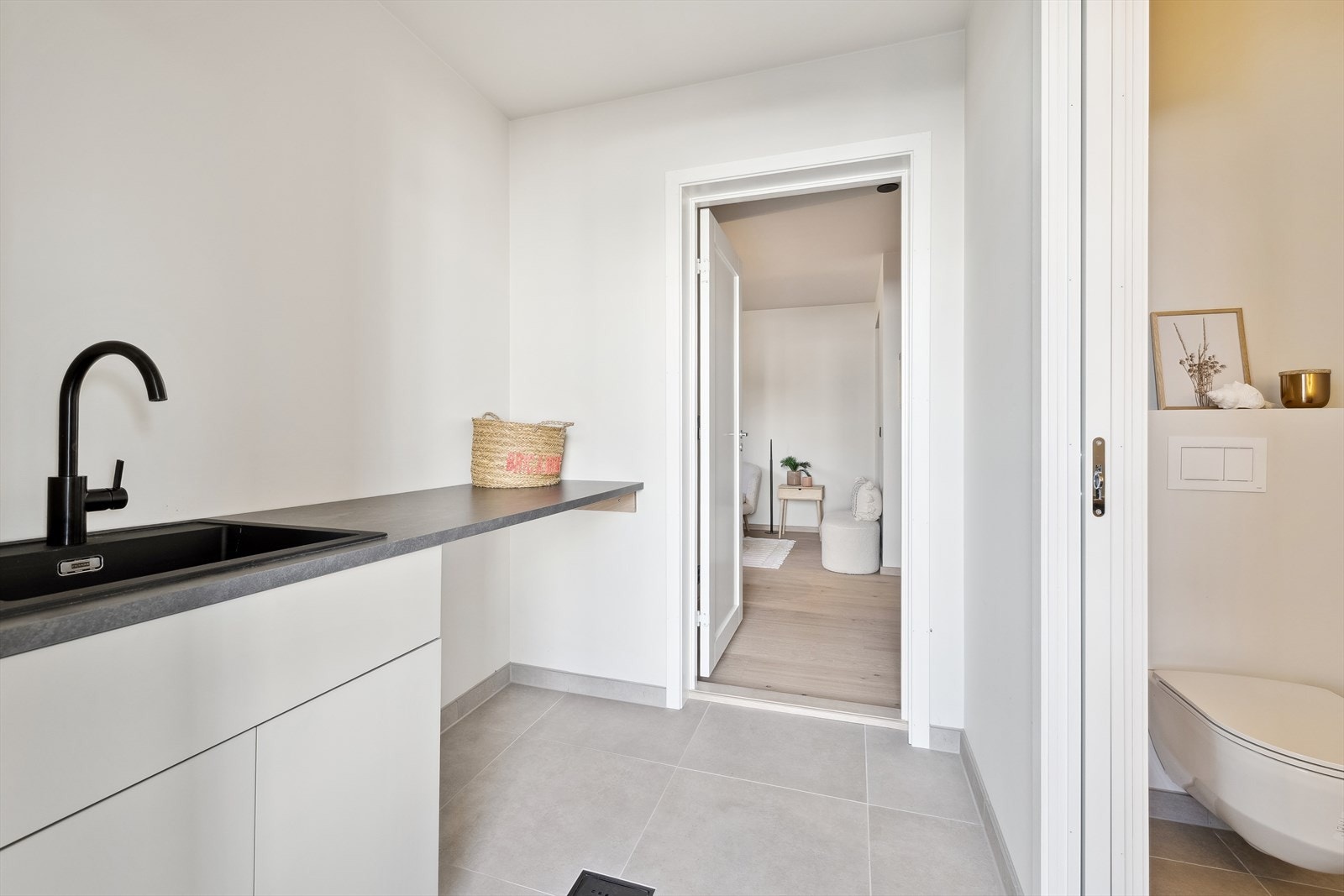 Vaskerommet har flislagt gulv med varmekabler og er innredet med benkeskap med stålvask og kran samt opplegg for vaskemaskin. Galleribilde