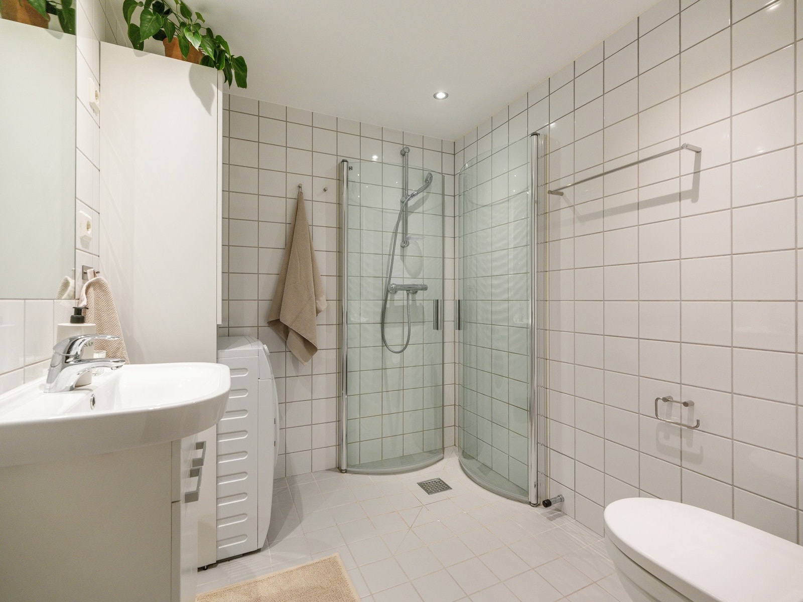 Baderommet har et tidløst utrykk med hvite fliser, Vegghengt toalett, dusjhjørne og servant med underskap. Galleribilde