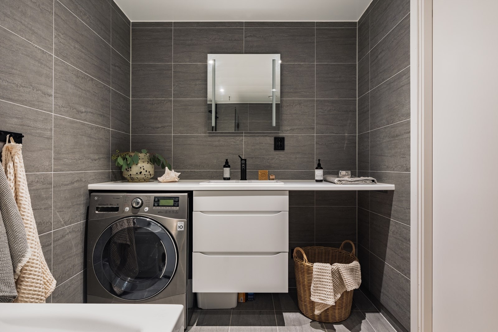 Badet er praktisk kombinert med vaskerom og har plass til både vaskemaskin og tørketrommel under benk, noe som gir en funksjonell og plassbesparende løsning. Galleribilde