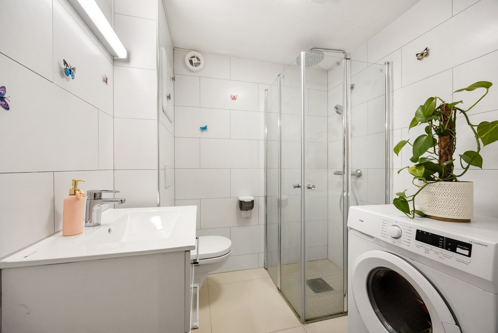 Badet er utstyrt med dusjhjørne med innfellbare glassvegger, vegghengt wc og servantinnredning med skuffer, samt opplegg og plass til vaskemaskin Galleribilde