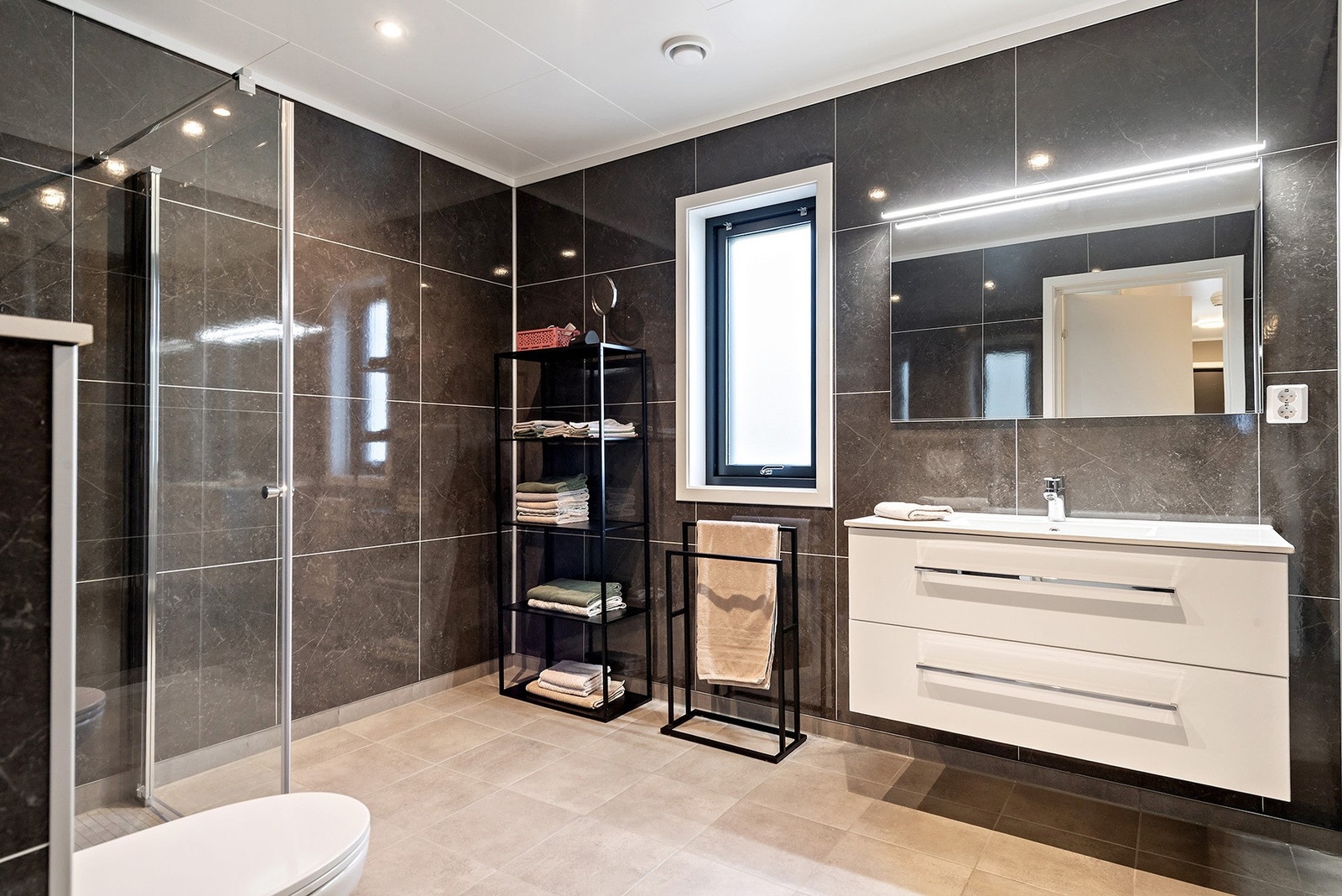 Boligen har ett romslig bad i 1. etasje med baderomspanel på vegger og fliser på gulv med gulvvarme. Galleribilde