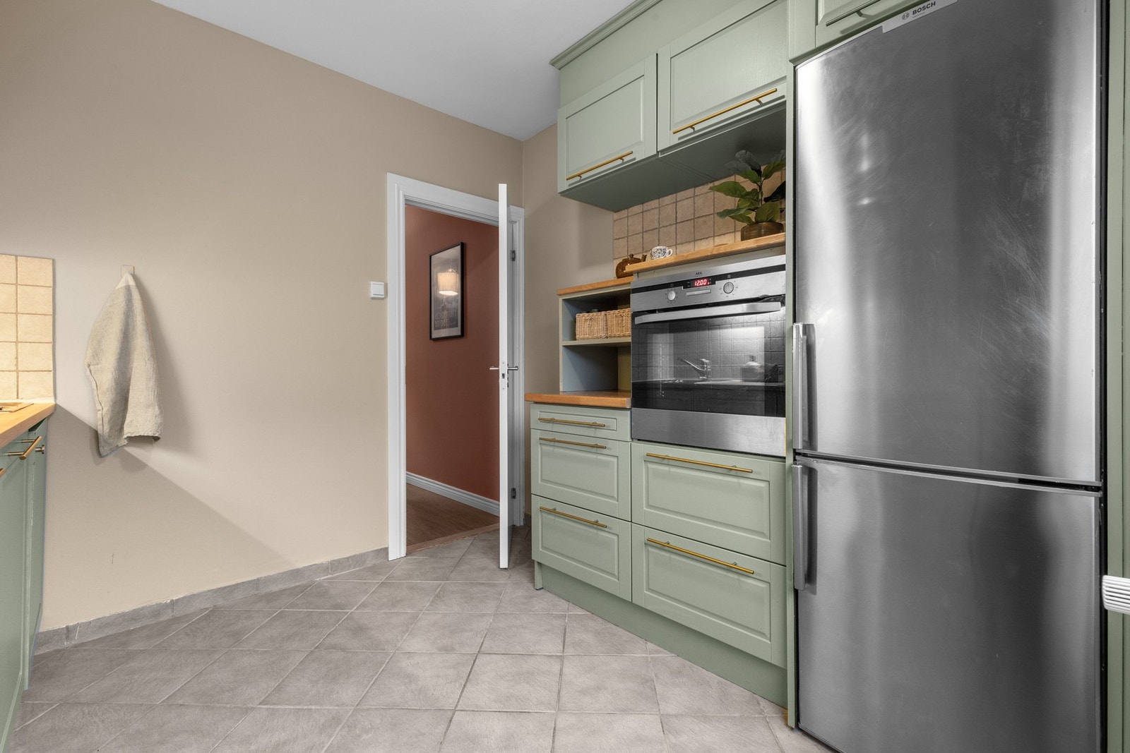 Velutstyrt kjøkken med nisje for kjøl-/fryseskap, innebygget stekeovn og oversiktlig planløsning som gir god flyt i hverdagen. Galleribilde