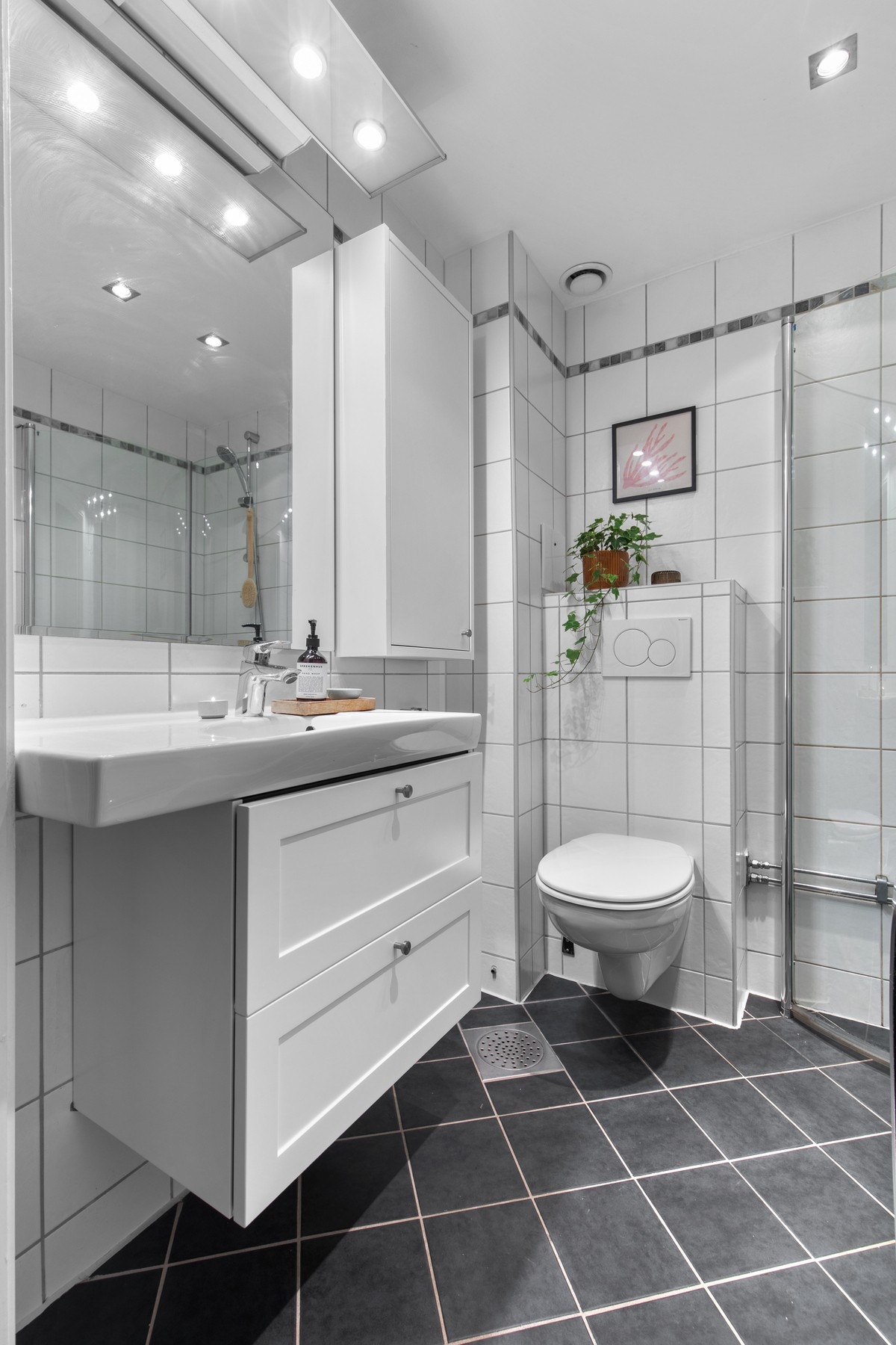 Moderne bad med vegghengt toalett, speil med belysning og praktisk opplegg for vaskemaskin - et gjennomtenkt rom for daglig bruk. Galleribilde