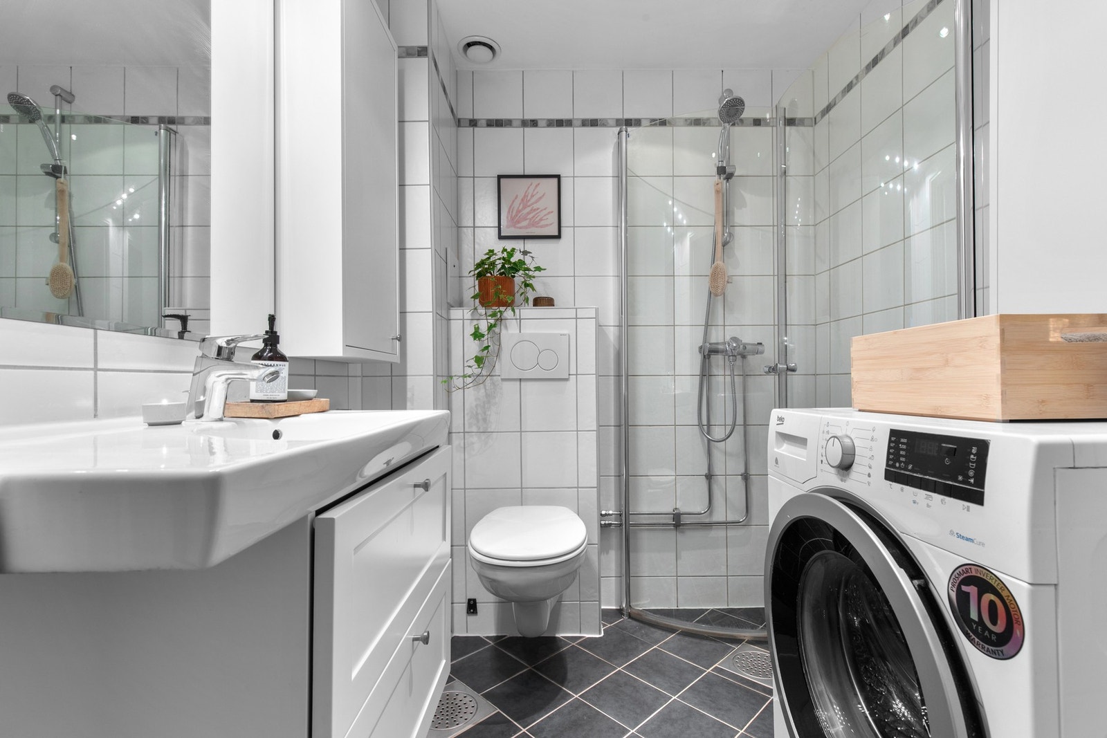 Pent flislagt bad med behagelige varmekabler i gulv, servantseksjon med skuffer og dusjhjørne med glassdører som gir et ryddig og funksjonelt uttrykk. Galleribilde