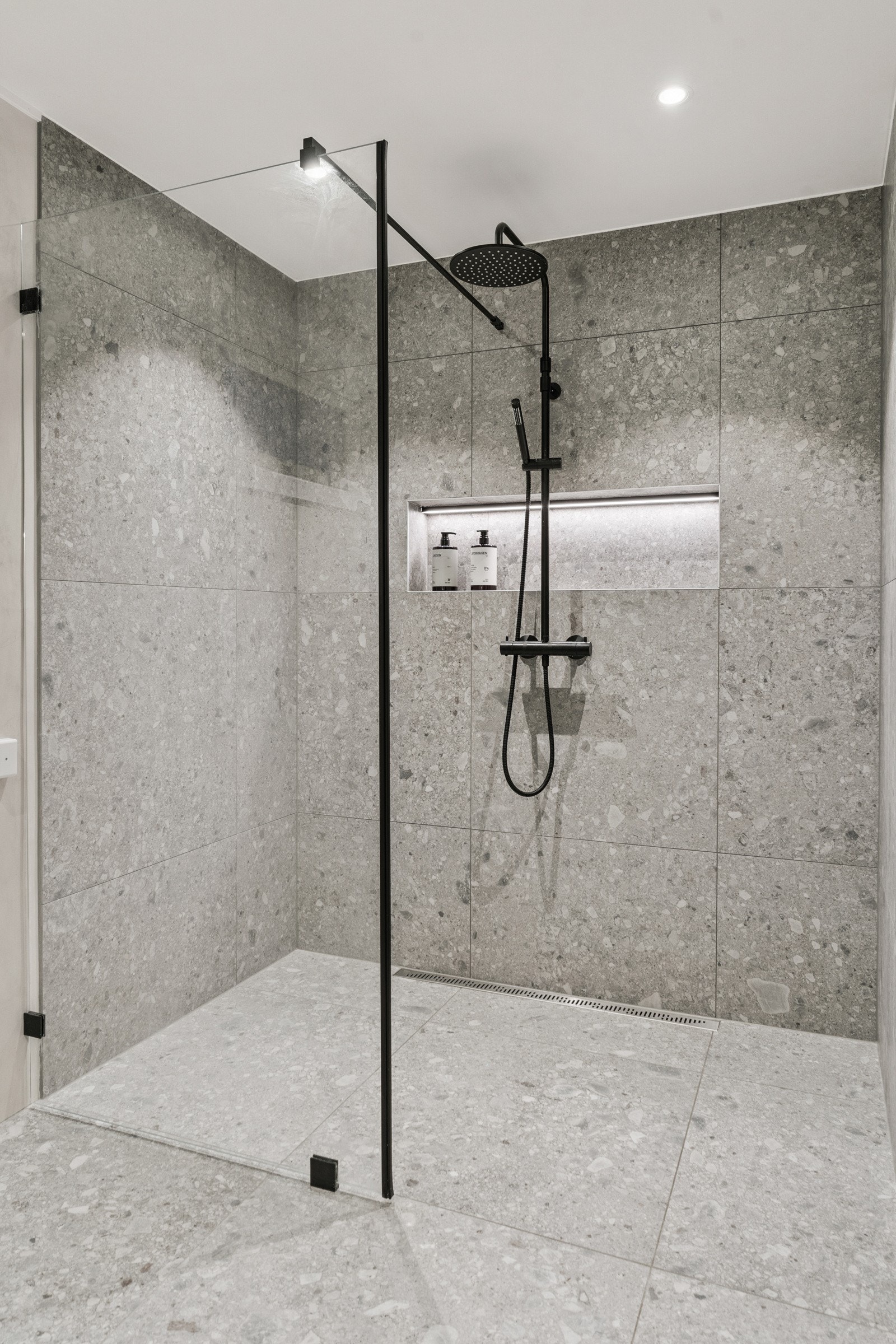 Dusjnisjen er romsleg og har store moderne fliser, regndusj og hylle med belysning. Svart dusjarmatur gjev eit stilfullt uttrykk Galleribilde