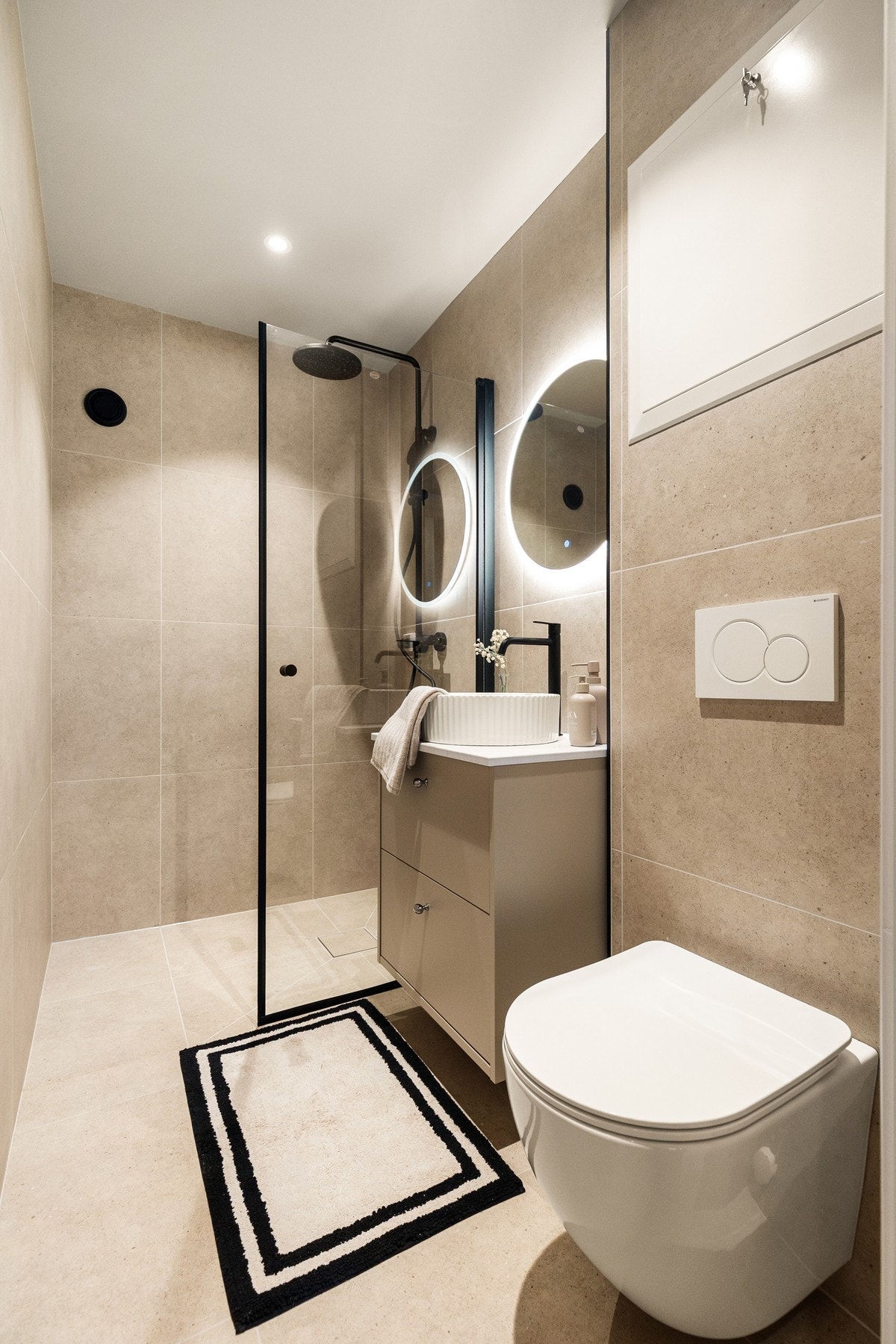 Delikat og moderne bad med flislagte overflater, veggmontert toalett og stilren dusjløsning med glassvegger. Galleribilde