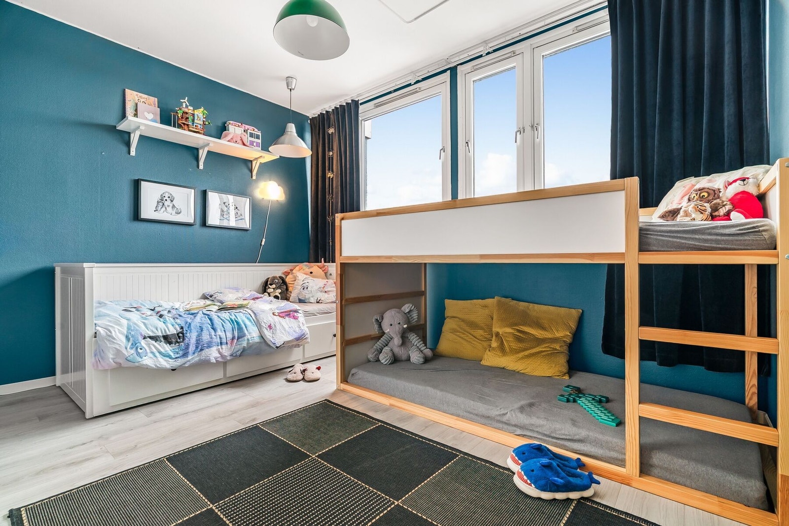 Boligens andre soverom er innredet som barnerom, malt i en rolig blåfarge og med store vinduer som gir godt innslipp av lys. Galleribilde