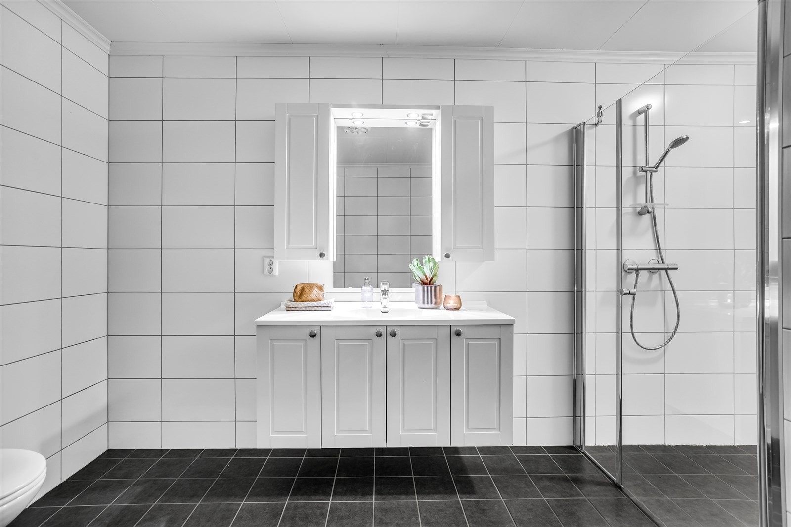 Baderomsinnredningen har hvite, profilerte fronter, overskap og speil med belysning. Galleribilde