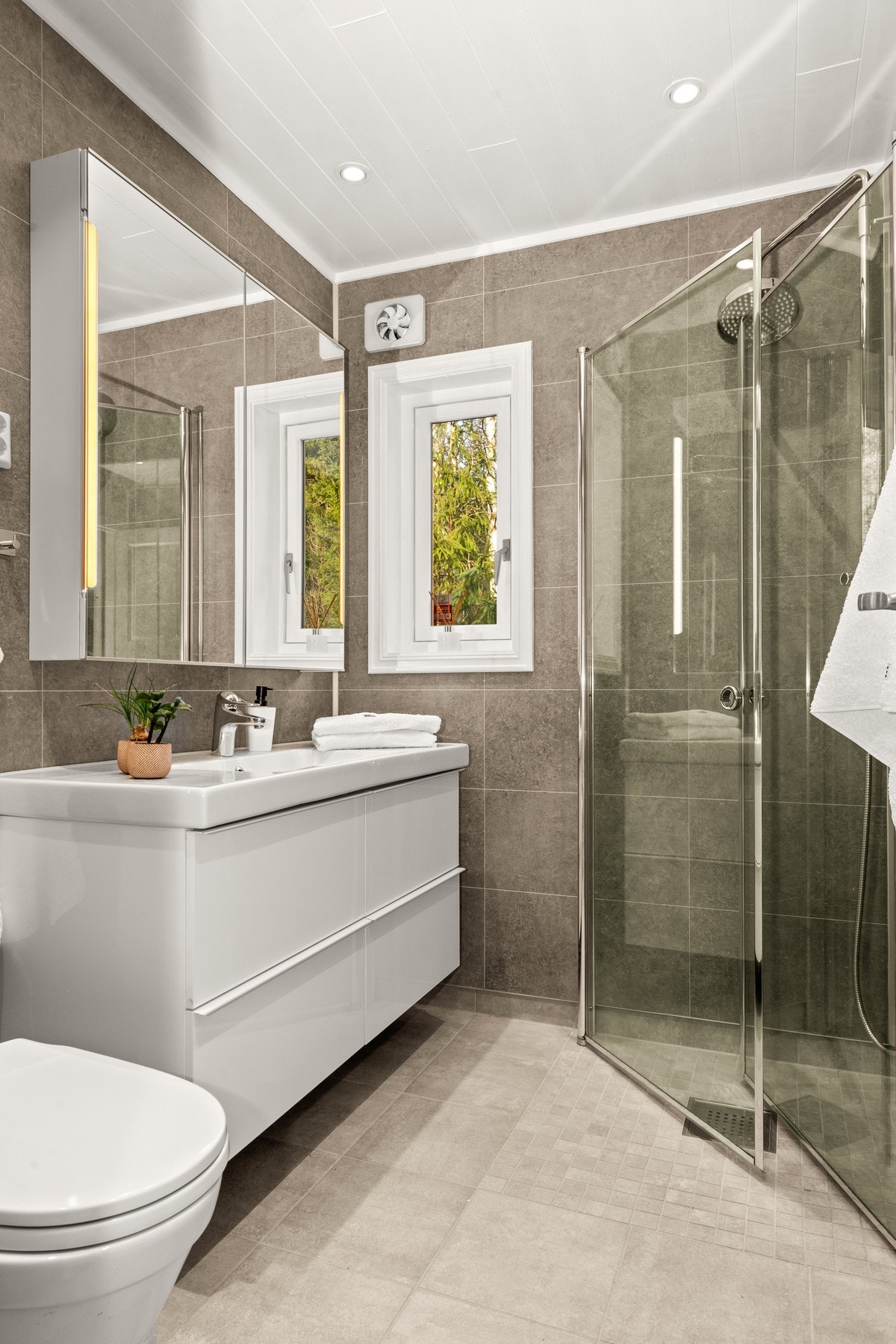 Rommet er innredet med dusjhjørne med takdusj og hånddusj, servantskap, speilskap og gulvstående wc. Galleribilde