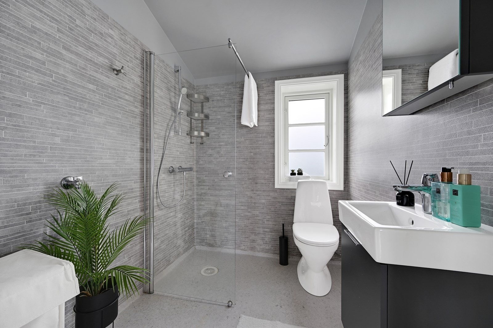 Bad/wc med sveiset belegg på gulv, våtromstapet på vegger, med dusj, servant med skuffer, speilskap, toalett og opplegg for vaskemaskin. Galleribilde