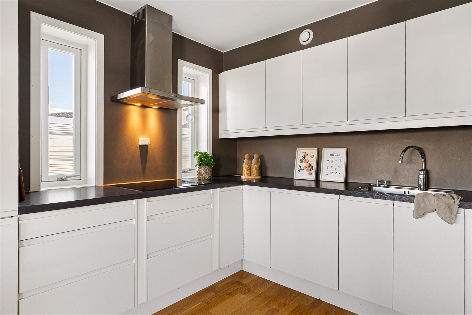 Innredningen har lyse, glatte fronter med integrerte håndtak, benkebelysning, ventilator og mørk benkeplate med nedfelt kum. Galleribilde