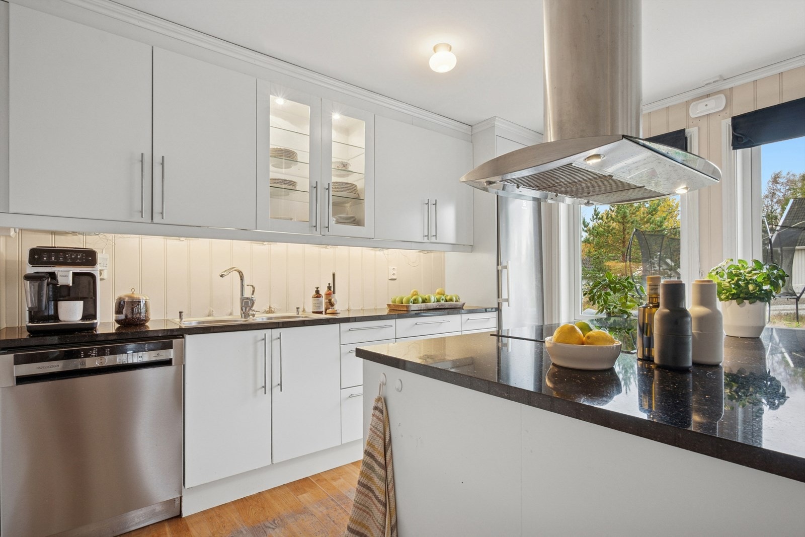 Kjøkkeninnredningen fremstår som pen og tidløs, med hvite, glatte fronter og mørke benkeplater i stein med nedfelt oppvaskkum i rustfritt stål. Galleribilde