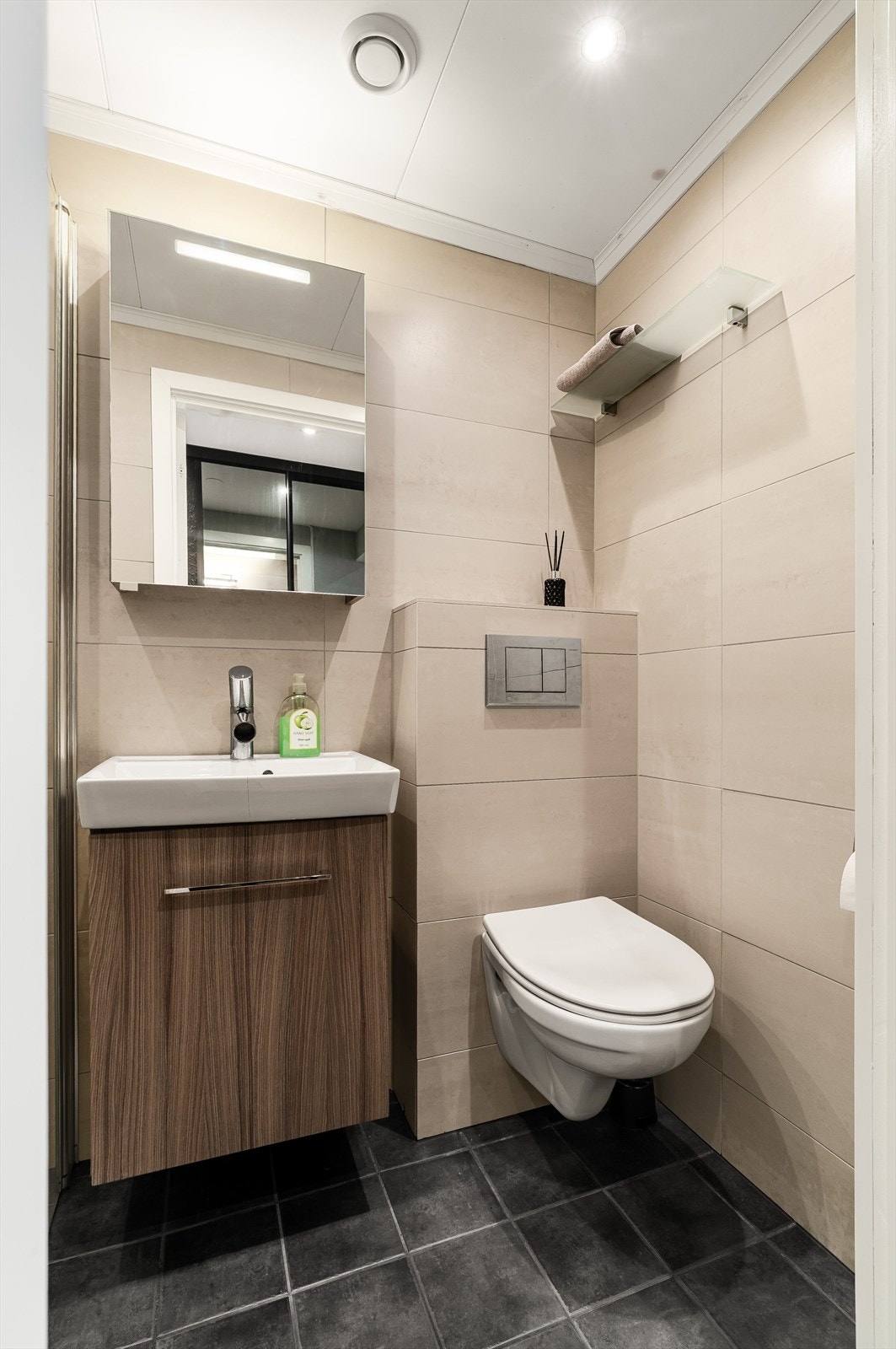 Flislagt bad fra 2012 med veggmontert toalett, innredet med servant på underskap og speilskap med hyller. Galleribilde