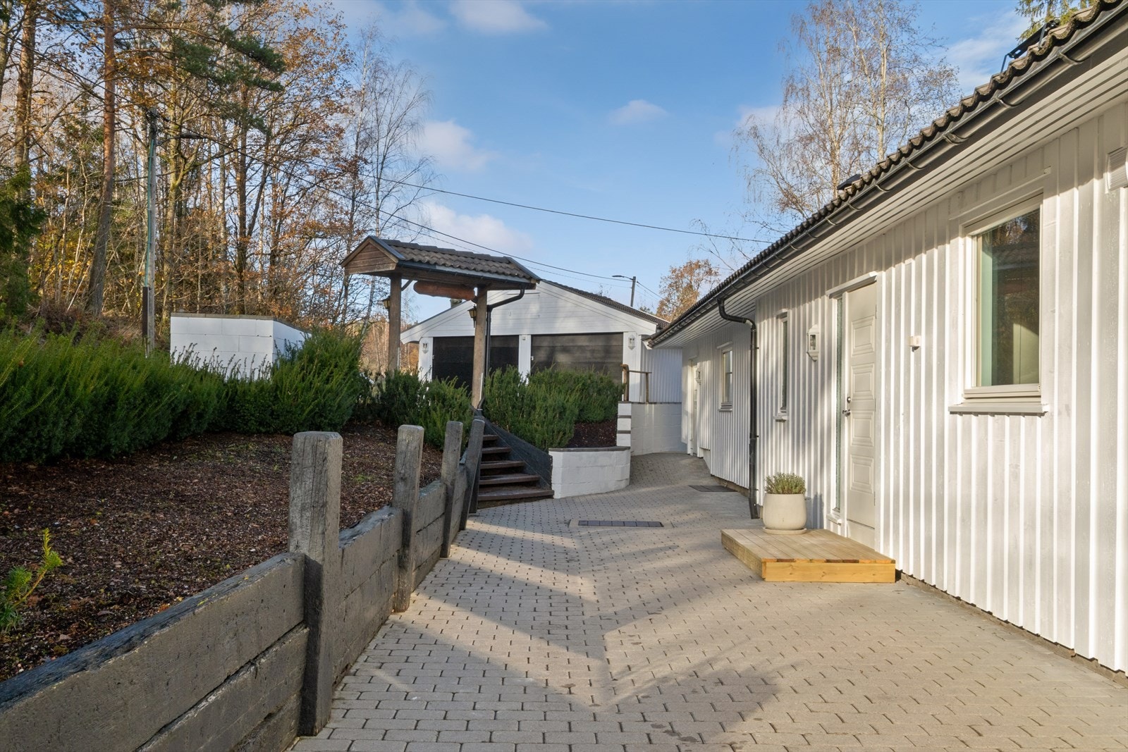 Huset har en asfaltert oppkjørsel og en overbygd terrasse med plasttak. Galleribilde