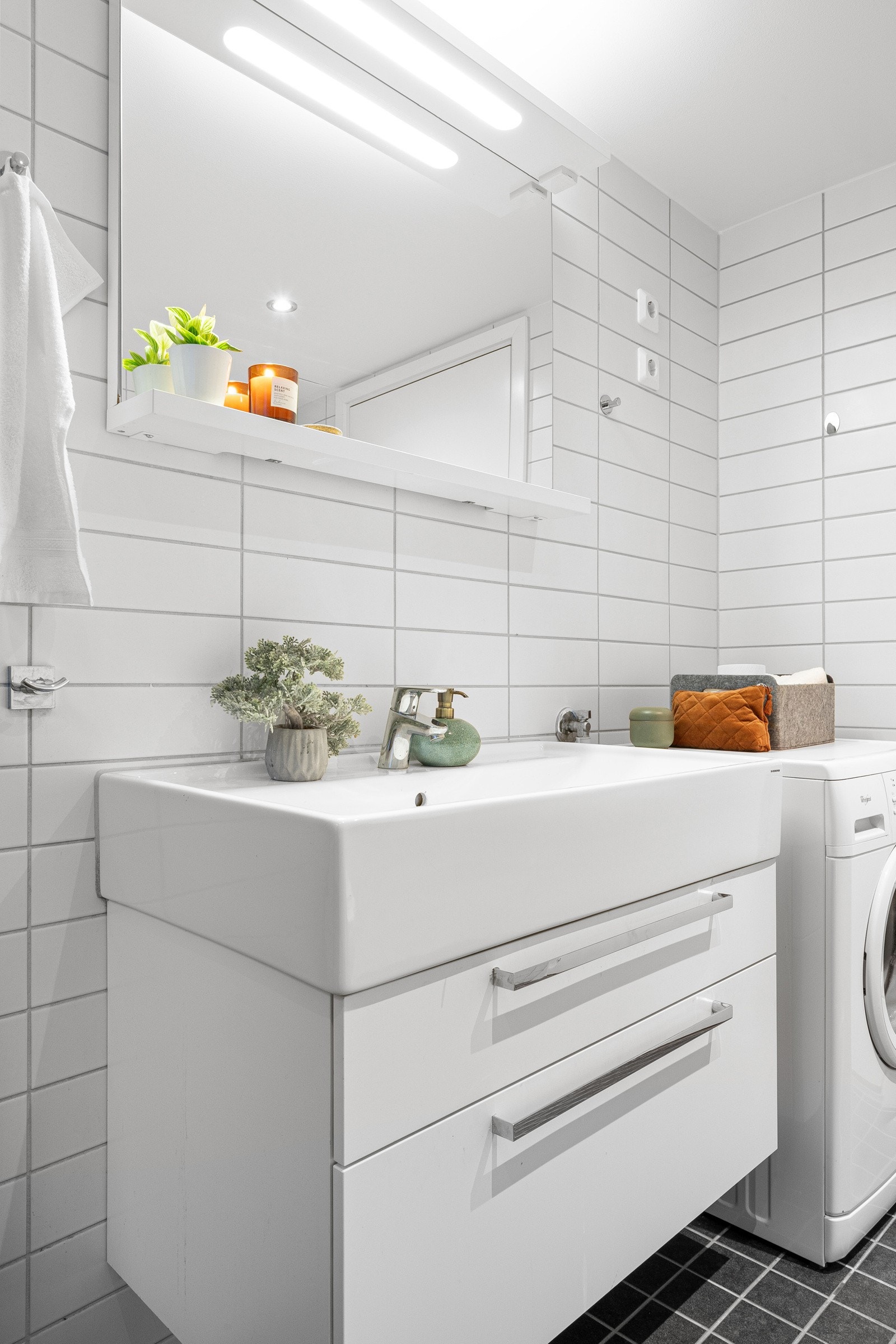 Baderommet har vegghengt servantskap med skuffer og ovenpåliggende servant med ett-greps armatur, speil med overlys, vegghengt toalett, samt dusjhjørne med glassdører og veggmontert dusjarmatur med hånddusj. Galleribilde