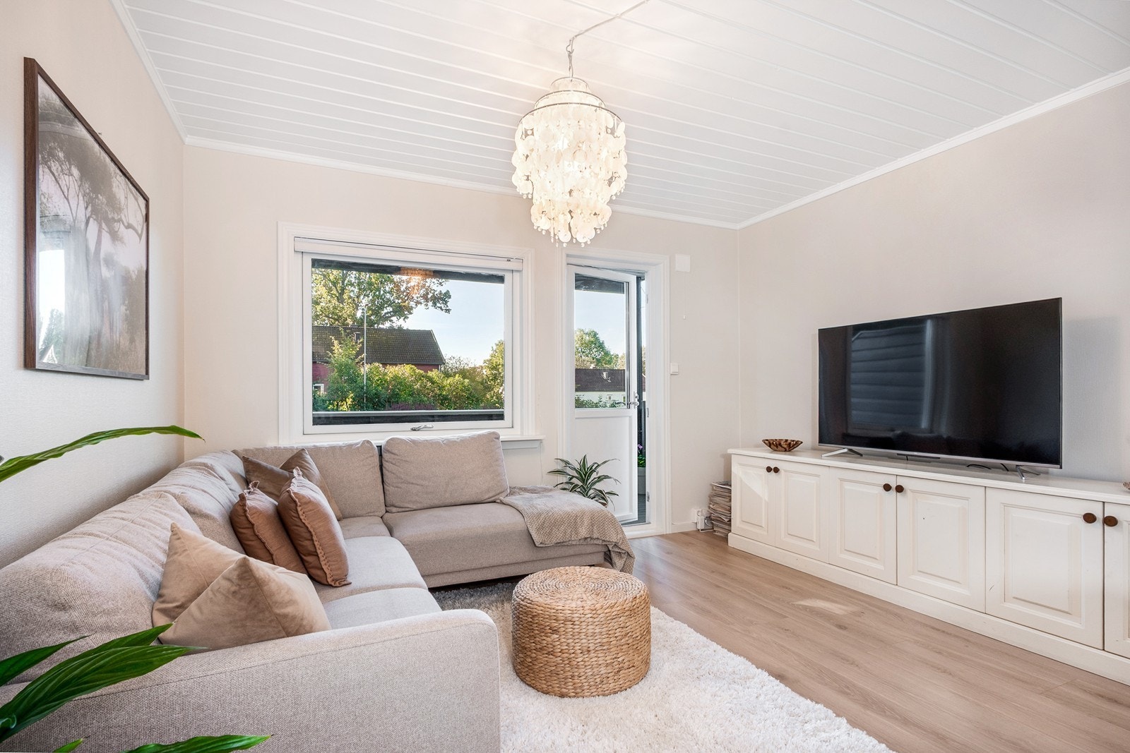 Sydvendte vindusflater slipper inn dagslys og er skjermet for innsyn, mens verandadøren leder ut til en solrik uteplass som fungerer som en naturlig forlengelse av stuen Galleribilde