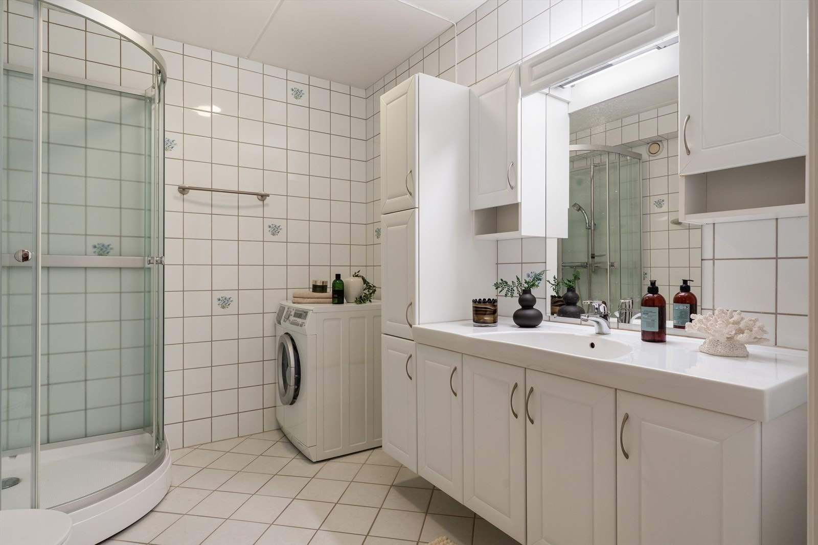 Rommet er innredet med nedfelt servant, speil, veggmonterte skap, toalett, dusjkabinett og opplegg for vaskemaskin. Galleribilde