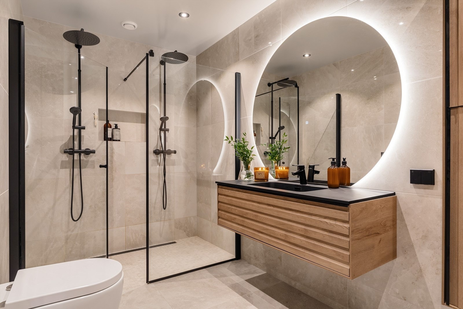 Badet fremstår som romslig og gjennomført med helhetlig materialbruk. Det er etablert dobbeldusj med separate dusjsoner, adskilt med glassvegger og utstyrt med moderne, sorte armaturer. Galleribilde