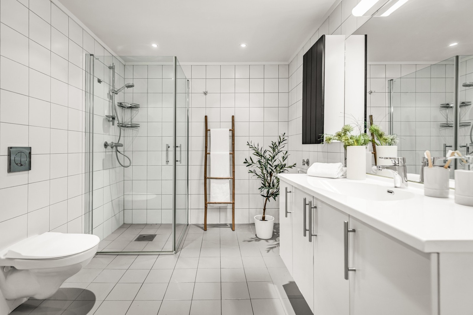 Badet er lyst og romslig med dusjhjørne, hvit innredning, veggmontert toalett og opplegg for vaskemaskin. Galleribilde