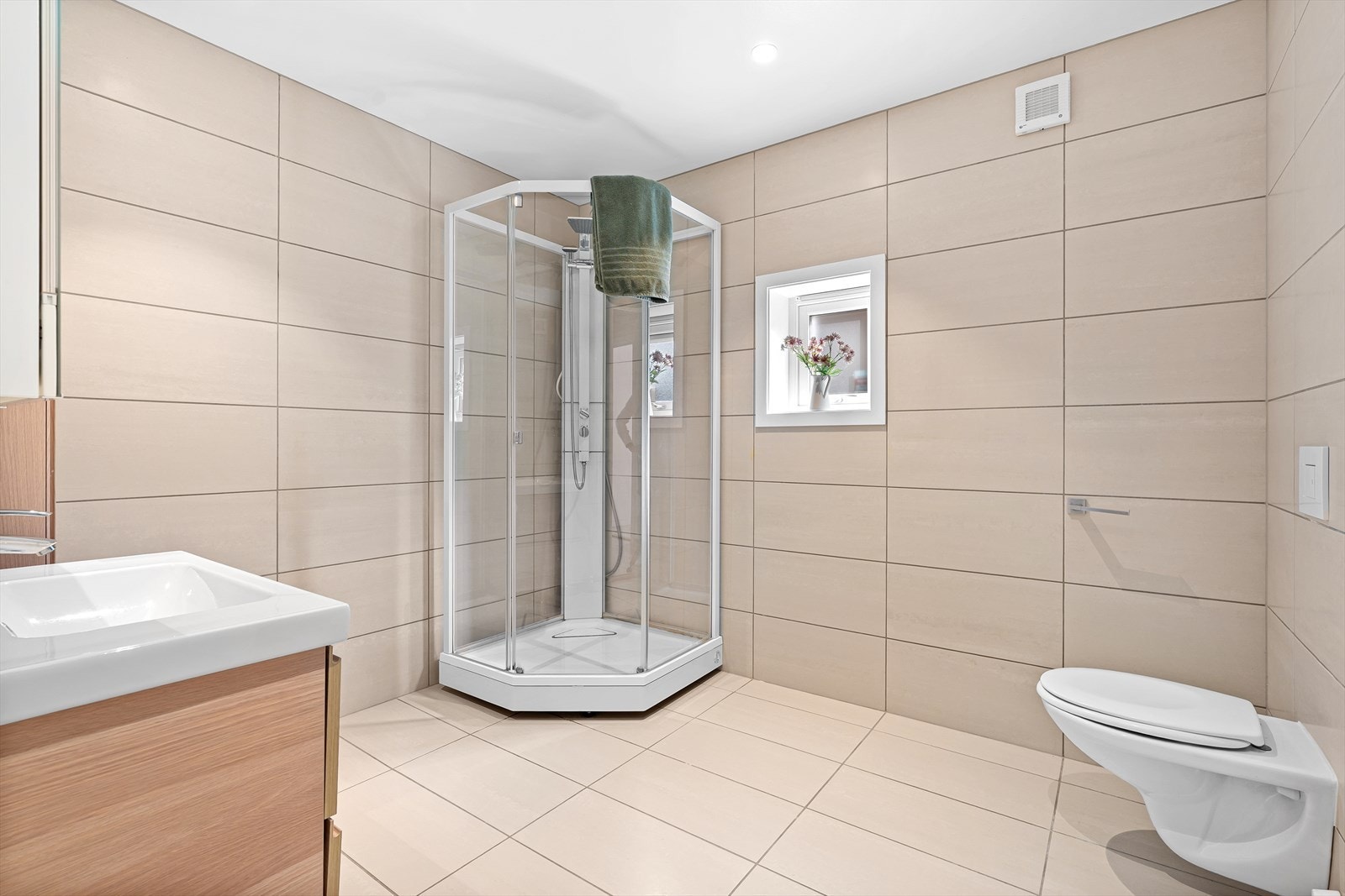 Badet er helfliset med varme i gulvet og inneholder et praktisk dusjkabinett, vegghengt toalett, samt baderomsinnredning med speil over. Galleribilde