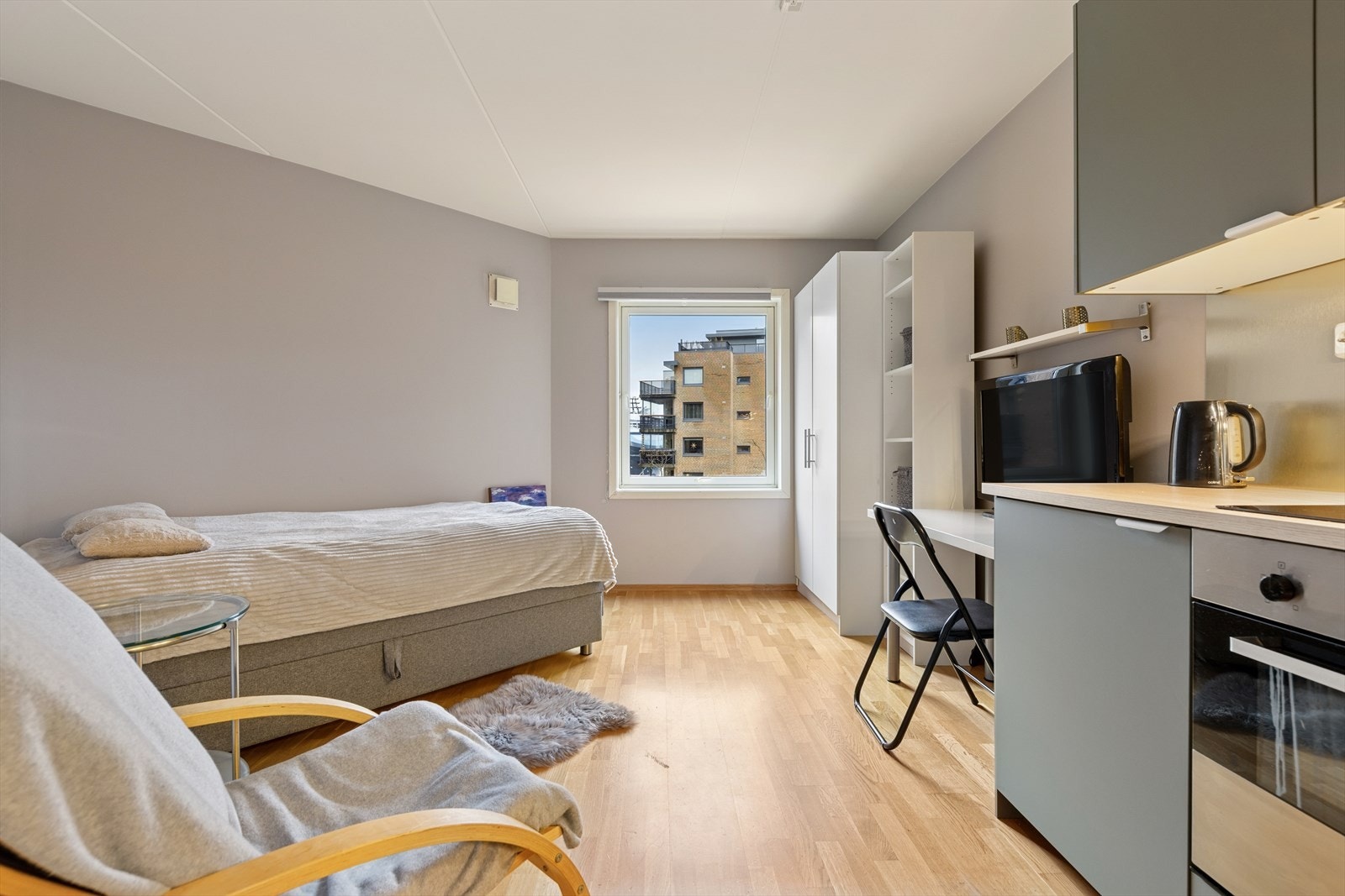 Hybel med lyst og praktisk oppsett, inkludert kjøkken, seng og stort vindu, malt i lyse toner som skaper et moderne og behagelig miljø Galleribilde